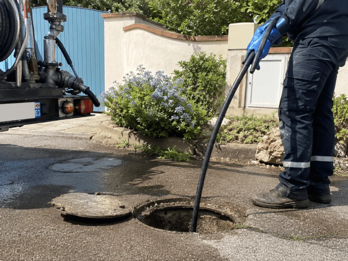 Debouchage d'un regard extèrieur devant une maison.png Homme qui effectué le débouchage d'une canalisation